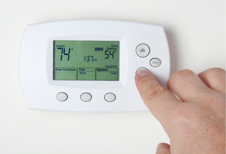 close up view of someone using a thermostat that shows the inside temperature at 74 degrees, the time at 1:37pm, and the cool temperature set to 54 degrees